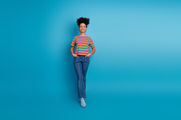 Young woman in casual striped shirt smiles confidently in front of a vibrant turquoise background,...