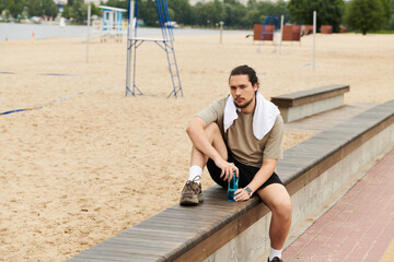 Young sporty man takes a break while working out by the beach in the evening sun