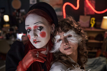 Portrait of two Caucasian teenage girls wearing creative makeup and costumes, one with mime face...