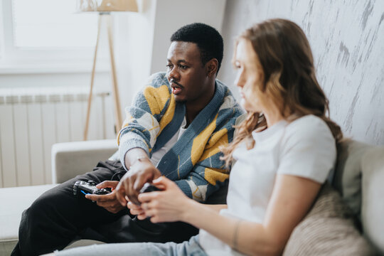A diverse couple sitting on a comfortable couch, engaging in a video game. The scene captures a warm and interactive atmosphere, emphasizing fun and connection.