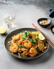 A delicious plate of Pad Thai with shrimp, tofu, peanuts, lime, and bean sprouts, garnished with fresh cilantro and chili flakes, ready to enjoy. AI