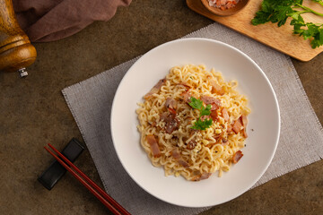 Instant noodle carbonara sauce topped with crispy bacon and parmesan cheese in white plate.Top view.