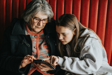 An elderly woman exploring a smart phone with the help of a younger woman, depicting inter...