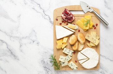 A variety of cheese and pomegranate seeds on a wooden board on marble background with copy space....