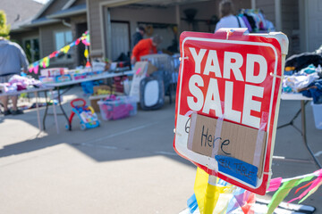 Selective focus on a yard sale sign with blurred tables of material 