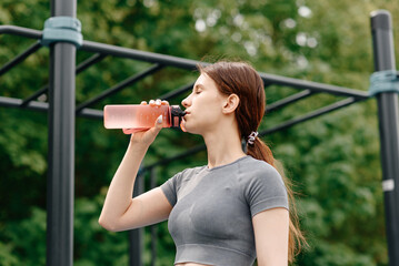 young woman stands on street sports ground before doing sport exercises outdoors in summer, drinks...