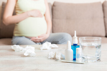 Attractive sick pregnant woman is lying in sofa. Taking pills from colds