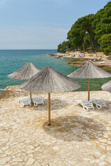 Sonnenschirme und Sonnenliegen an einer typischen Bdestelle am Strand von Porec an der kroatischen Küste der Adria