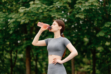 young woman stands on street sports ground before doing sport exercises outdoors in summer, drinks...