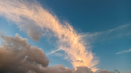 Naklejka premium A glowing streak of golden clouds stretches diagonally across a tranquil blue sky, with soft grey clouds below, creating a calm and majestic sunset scene.