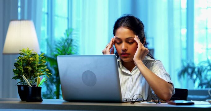 Indian businesswoman having headache while working on laptop at desk in modern cozy office, Asian young female showing stress and stiff neck symptoms while dealing with workload and physical pressure