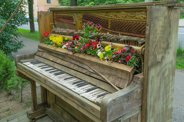 Old piano transformed into a vibrant flower garden on a city street. Urban art installation...