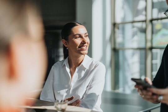 A cheerful businesswoman in a white shirt enjoys a conversation in a bright office kitchen, fostering a welcoming and collaborative atmosphere. Ideal for business, teamwork, and professional