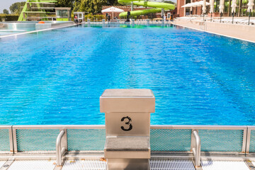 Empty swimming start block at outdoor pool under summer sun, with deep blue water and clean...