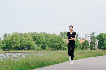 young slim beautiful caucasian woman running on path on river embankment in city park, black...