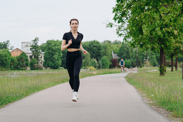 young slim beautiful caucasian woman running on path on river embankment in city park, black...