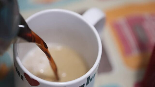 Caf&eacute; sendo colocado dentro de uma x&iacute;cara de cor branca misturando caf&eacute; com leite em camera lenta. 