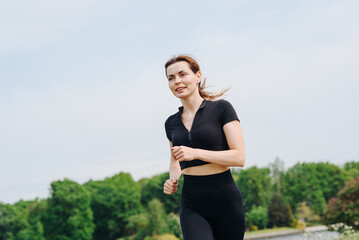 young slim beautiful caucasian woman running on path on river embankment in city park, black...