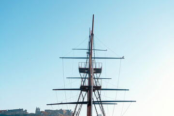 Tall ship mast reaches toward clear blue sky in coastal city harbor showcasing maritime tradition...
