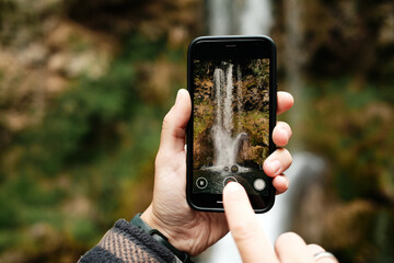 Hands holding smartphone filming Veliki Buk waterfall in Lisine reserve, Serbia. Natural wonder...