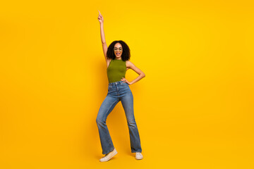 Cheerful young woman in casual style posing against a vibrant yellow background in a green top and...