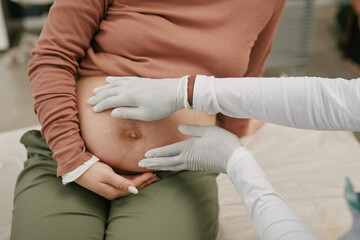 Asian pregnant woman sitting during prenatal checkup with medical professional examining abdomen...