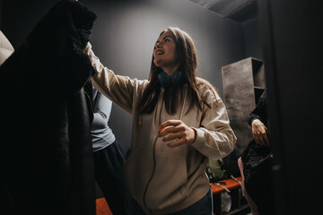 A young woman wearing headphones and a hooded sweatshirt is seen selecting clothing in a...