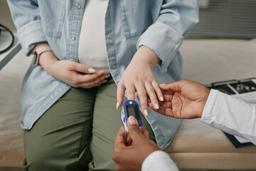 Pregnant Asian woman sitting during prenatal care checkup having hand examined by medical...