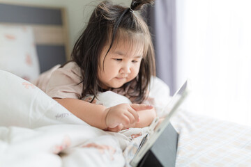 A little Asian girl is lying on the bed watching a tablet,Asian girl lying on bed in bedroom and...