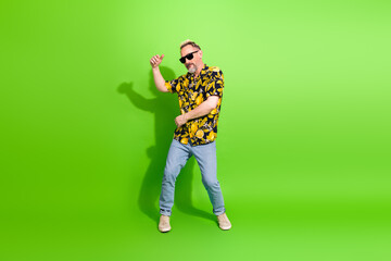 Stylish mature man in vibrant summer shirt and sunglass dancing joyfully against a vivid green...