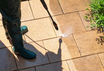 A person removes tough dirt from patio tiles using a high-pressure washer. Clear before-and-after effect