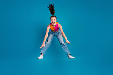 Energetic girl in vibrant outfit jumps against a blue background exuding fun and joyful emotions
