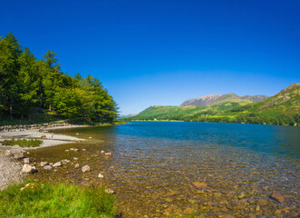 Naklejka premium Gravel lakeshore with clear water and mountains in summer (Buttermere, Lake District, England, United Kingdom)