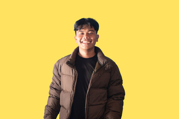 Smiling Young Man in Brown Puffer Jacket Against Yellow Background