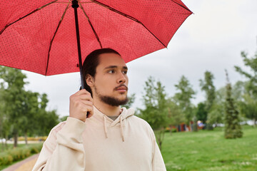 Sporty young man enjoying outdoor time in hoodie under a bright umbrella