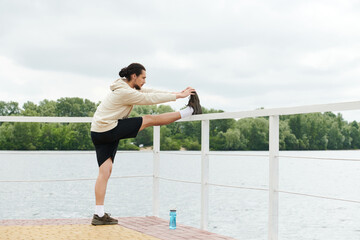Sporty young man stretches by the water in a serene outdoor setting