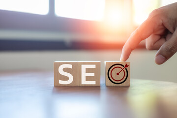 Hand arranging wooden blocks forming the word SEO with a target icon,