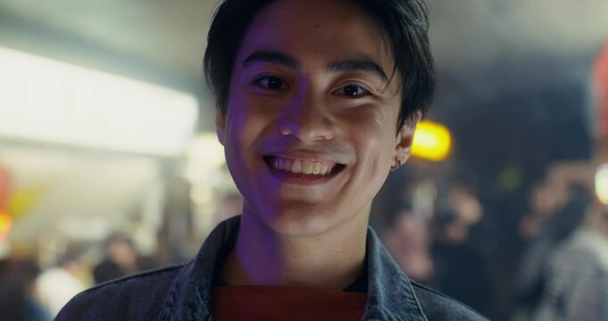 A young man smiles looking at the camera while standing outdoors. Close-up of his face