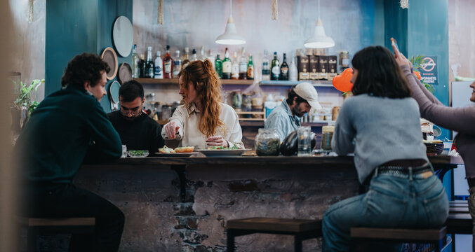 Group of friends socializing and eating at a bar with a relaxed atmosphere, enjoying the ambiance and shared moments. The setting is vibrant and showcases a welcoming and friendly environment.
