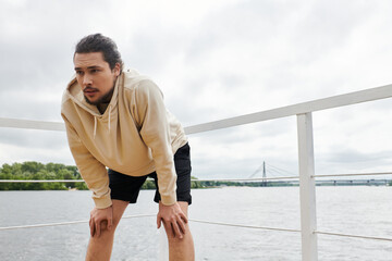 Sporty young man focuses on his workout by the river on a cloudy day