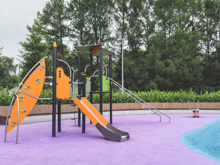 Modern playground with orange slide and climbing structures on vibrant purple and blue rubber...