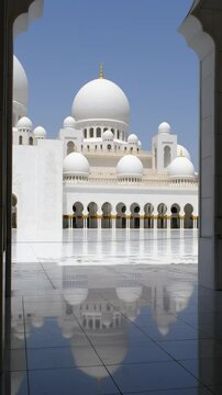 A stunning view of a white mosque&rsquo;s domes and arches with golden accents, reflected on shiny tiled flooring on a bright, sunny day.