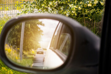 A car is driving down a road and the rear view mirror shows a truck