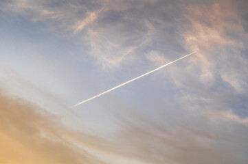 white trace of the plane in the blue sky with soft clouds