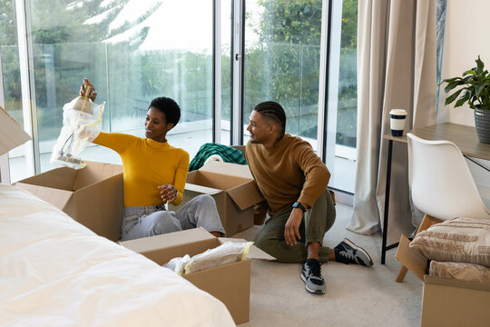 Unpacking Diverse couple opening bubble-wrapped lamp on bedroom floor, with cardboard boxes