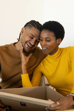 Opening couple examining box contents on sofa, wearing brown quilted shirt and yellow turtleneck