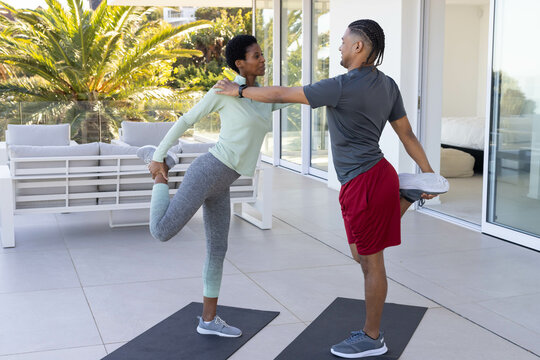 Stretching Diverse workout partners in sportswear holding ankles behind on terrace, with yoga mats