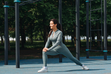 young athletic caucasian woman doing stretching exercises outdoors in summer, grey sportswear,...