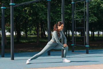 young athletic caucasian woman doing stretching exercises outdoors in summer, grey sportswear,...