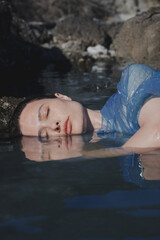 Artistic close-up portrait of a brunette woman with closed eyes, wearing a transparent plastic raincoat on her body.